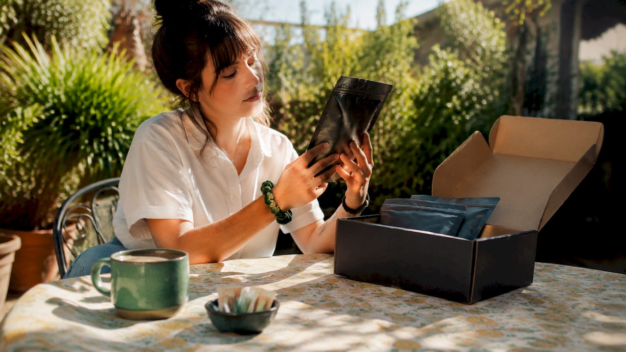 Woman unboxing coffee subscription at kitchen table