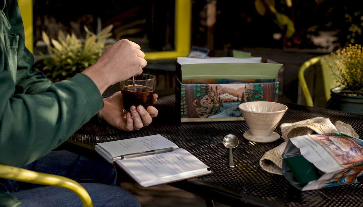 Hands swirling coffee in glass over wooden table